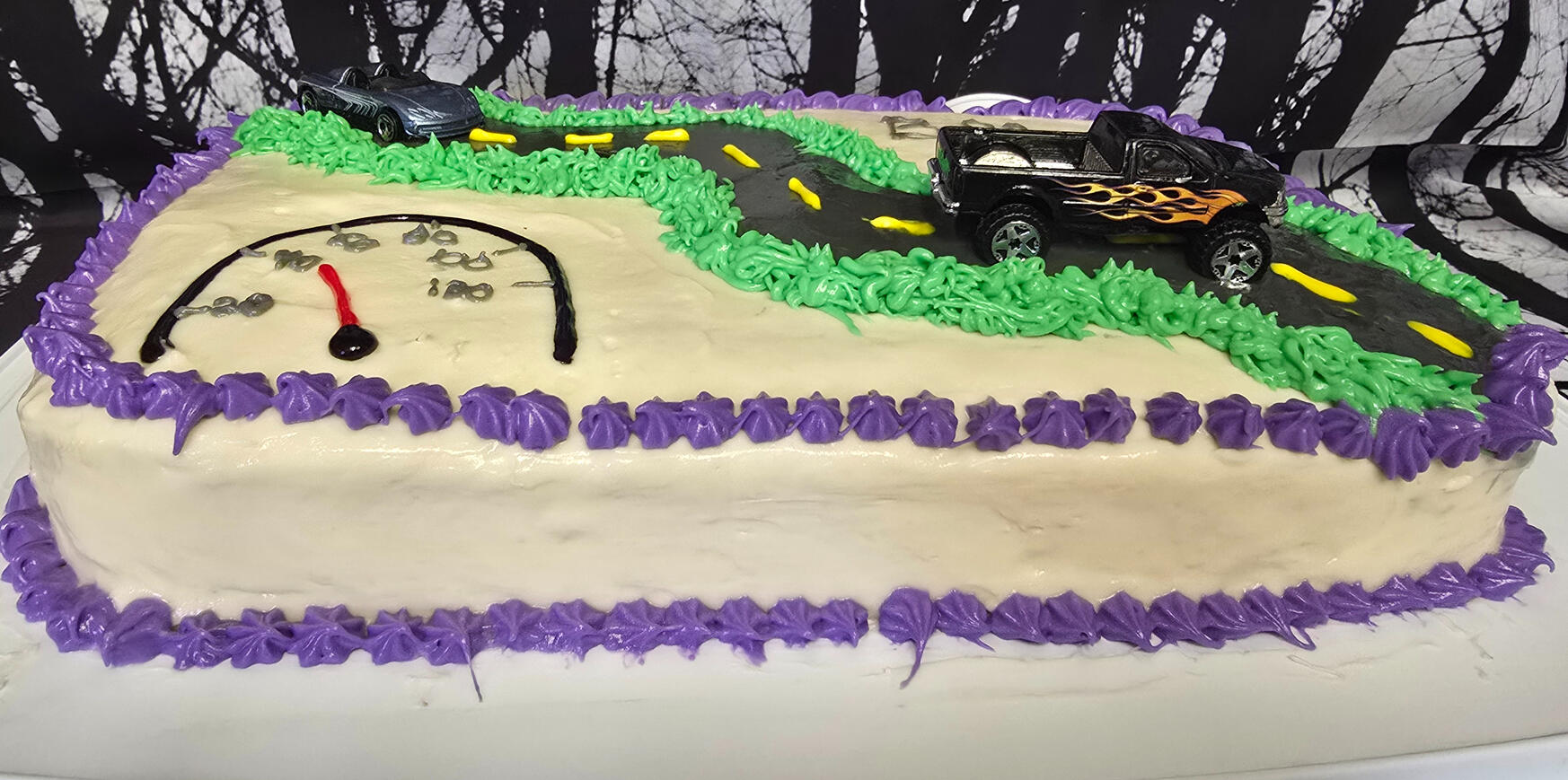Race car sheet cake with racetrack design Race car sheet cake with a frosted racetrack, toy car, and speedometer design